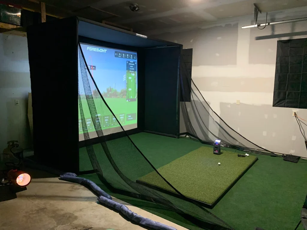 Bushnell Launch Pro SIG10 simulator setup in a garage with Foresight software displayed on the impact screen and side netting