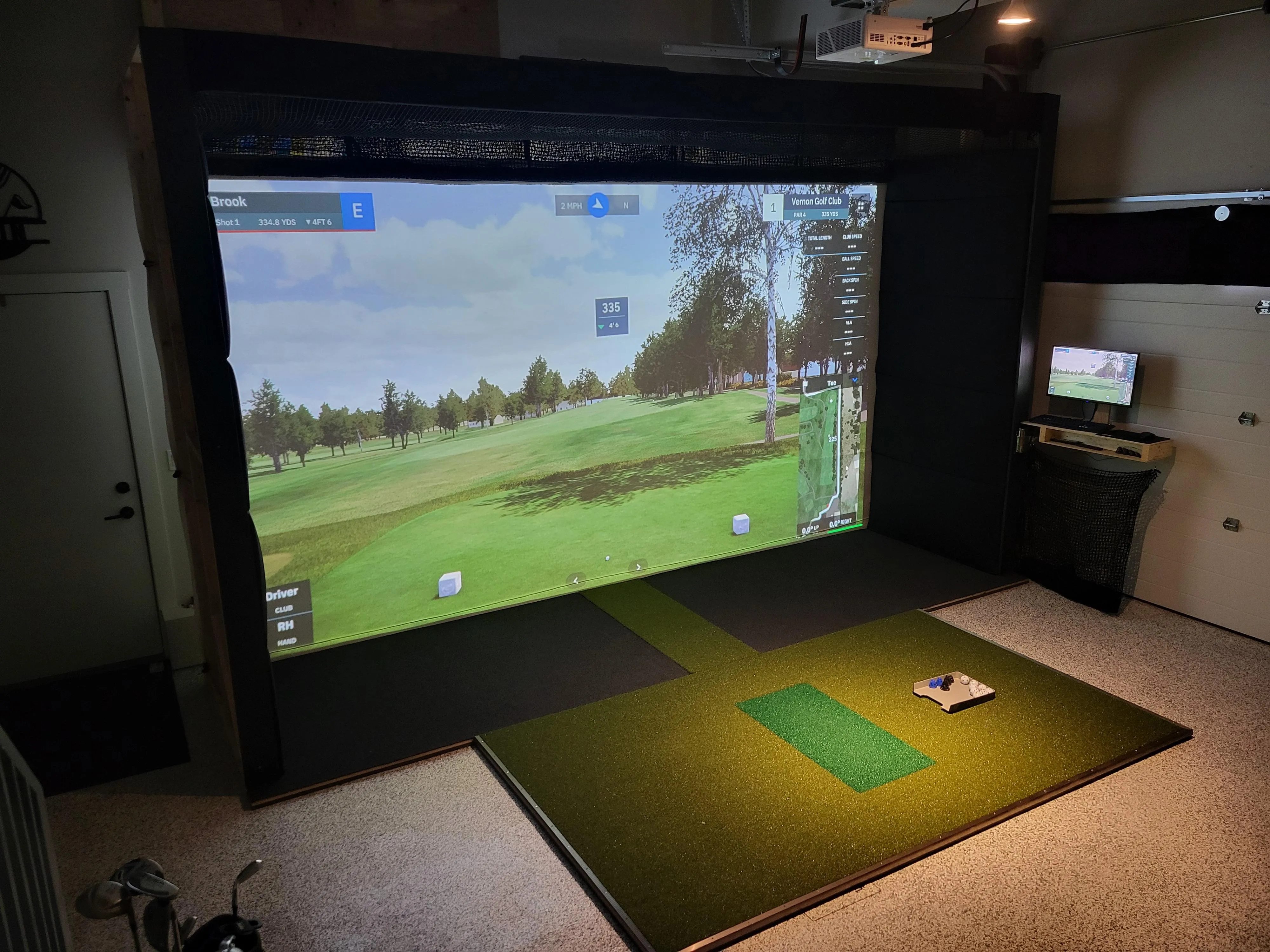 TrackMan iO SIG10 golf simulator package installed in a home garage with impact screen, hitting mat, and side monitor