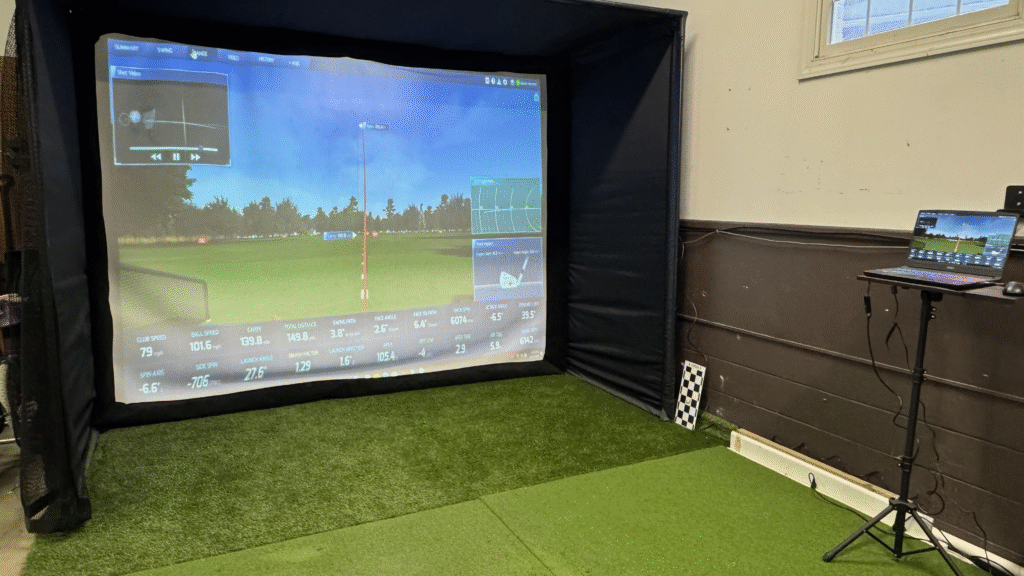 ProTee VX SwingBay golf simulator package with overhead launch monitor, impact screen showing ball flight data, and laptop for tracking
